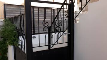 A black metal gate with intricate designs, leading to a staircase with a stone wall on one side and a beige wall on the other.