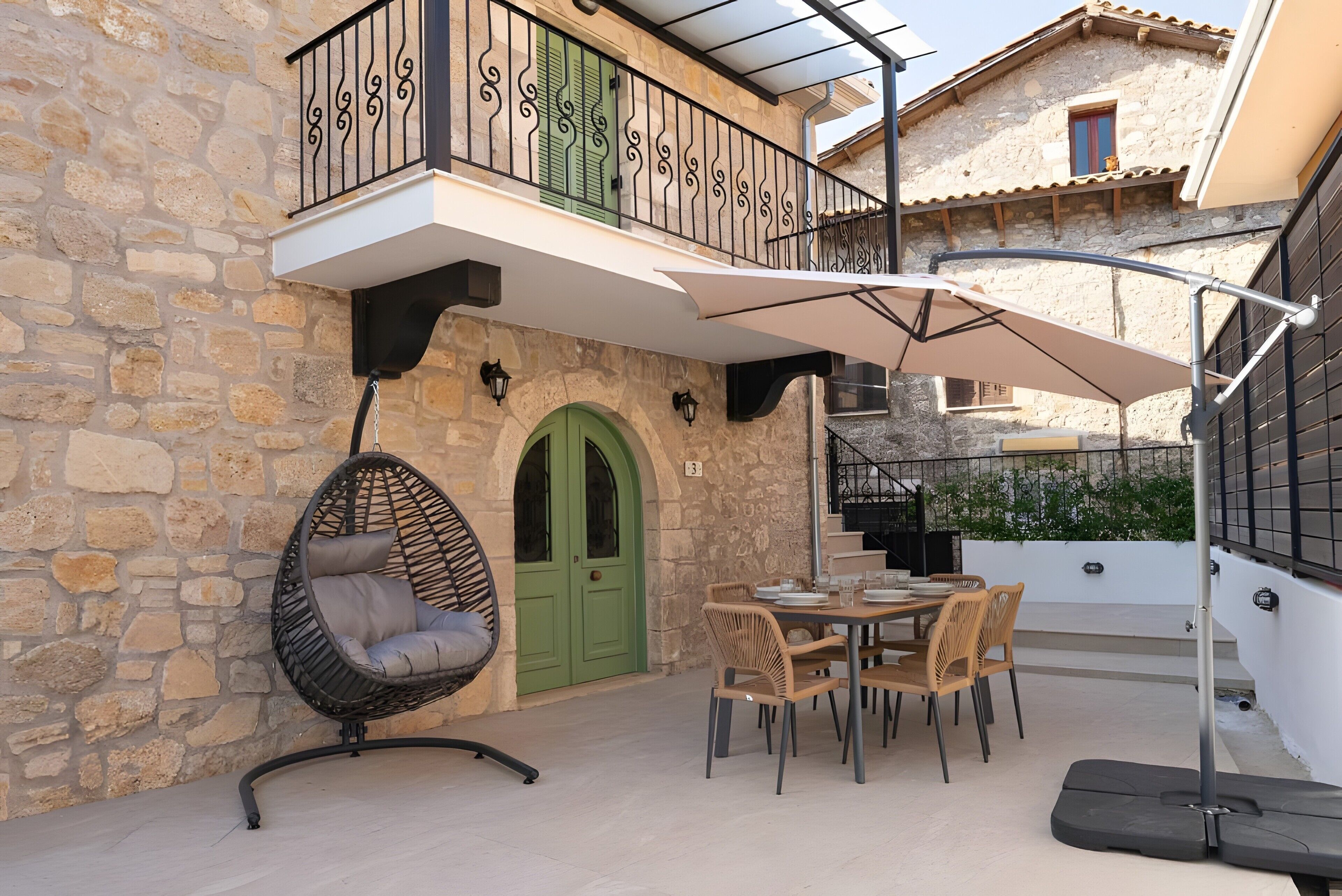 A stone building with a green door, a balcony with a metal railing, and outdoor furniture including a table and chairs.