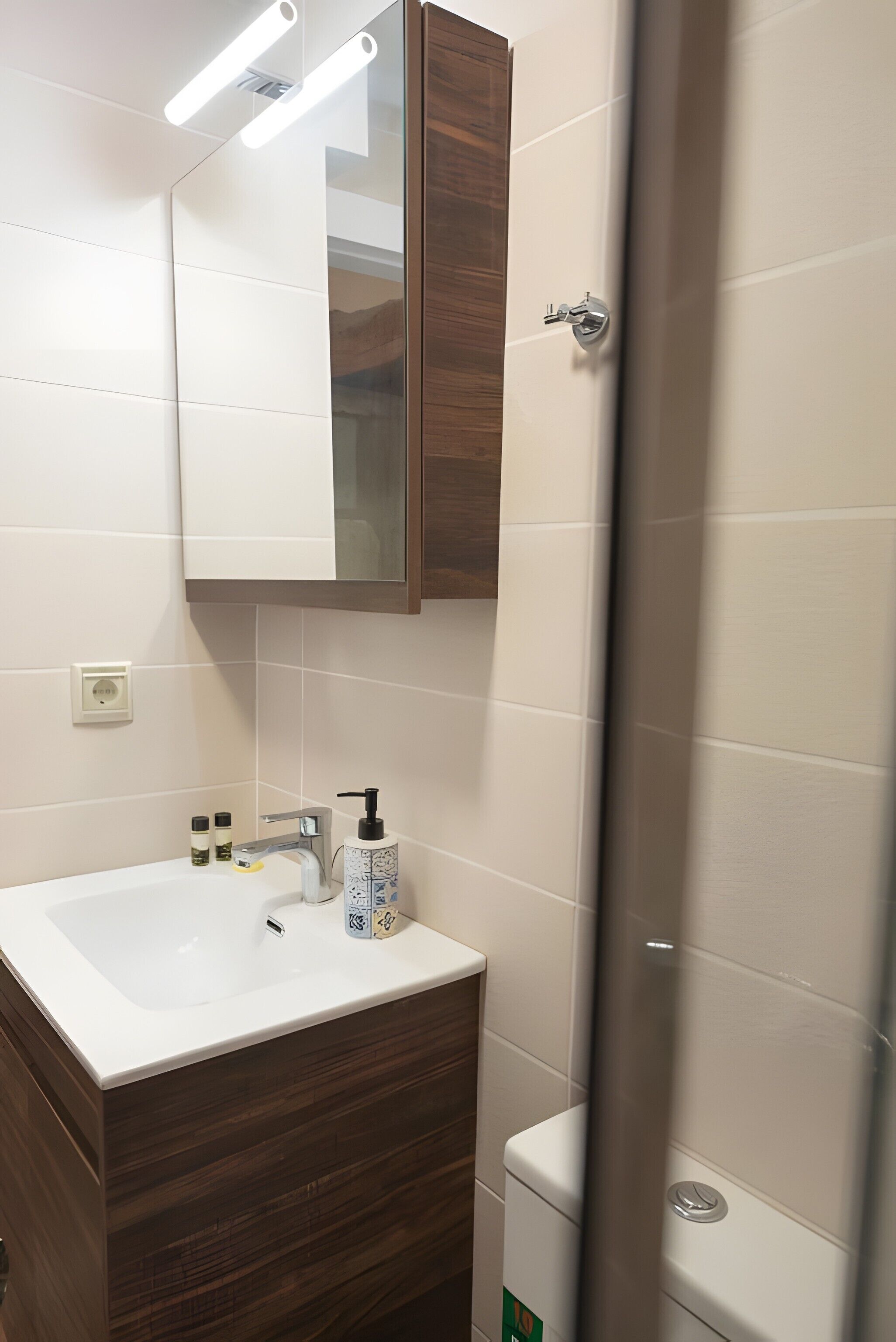 Un baño con lavamanos blanco, tocador de madera, un espejo y cortina de ducha.