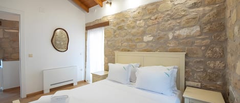 A bedroom with a stone wall, a wooden ceiling, a bed with white linens, and a nightstand with a lamp.