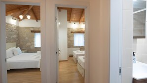 Une chambre d’hôtel avec un mur en pierre, un plafond en bois et un lit recouvert de draps blancs.