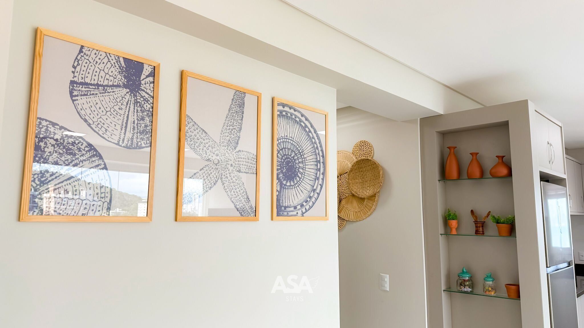 Une cuisine moderne agrémentée de trois œuvres d’art encadrées accrochées au mur, d’un réfrigérateur et d’étagères ornées d’objets décoratifs.