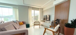 A modern living room with a sofa, armchair, and a TV on a stand. - ASA Vista Mar 3QT Alto Padrao Itapema (Itapema)