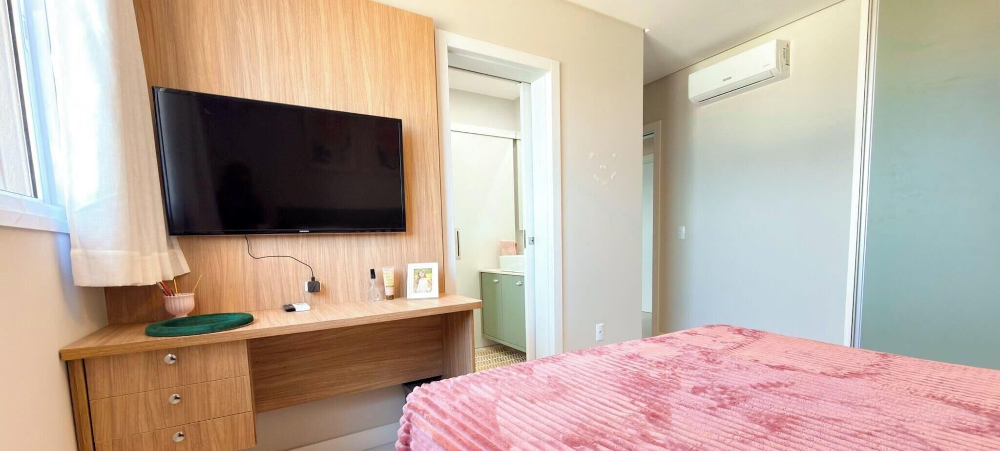 Ein Schlafzimmer mit einem Bett, einem an einer Holzeinrichtung montierten Fernseher, einer grünen Ablage und einer Tür zu einem anderen Raum.