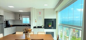 A modern kitchen with a dining area, large windows, and a view of the city. - ASA Vista Mar 3QT Alto Padrao Itapema (Itapema)