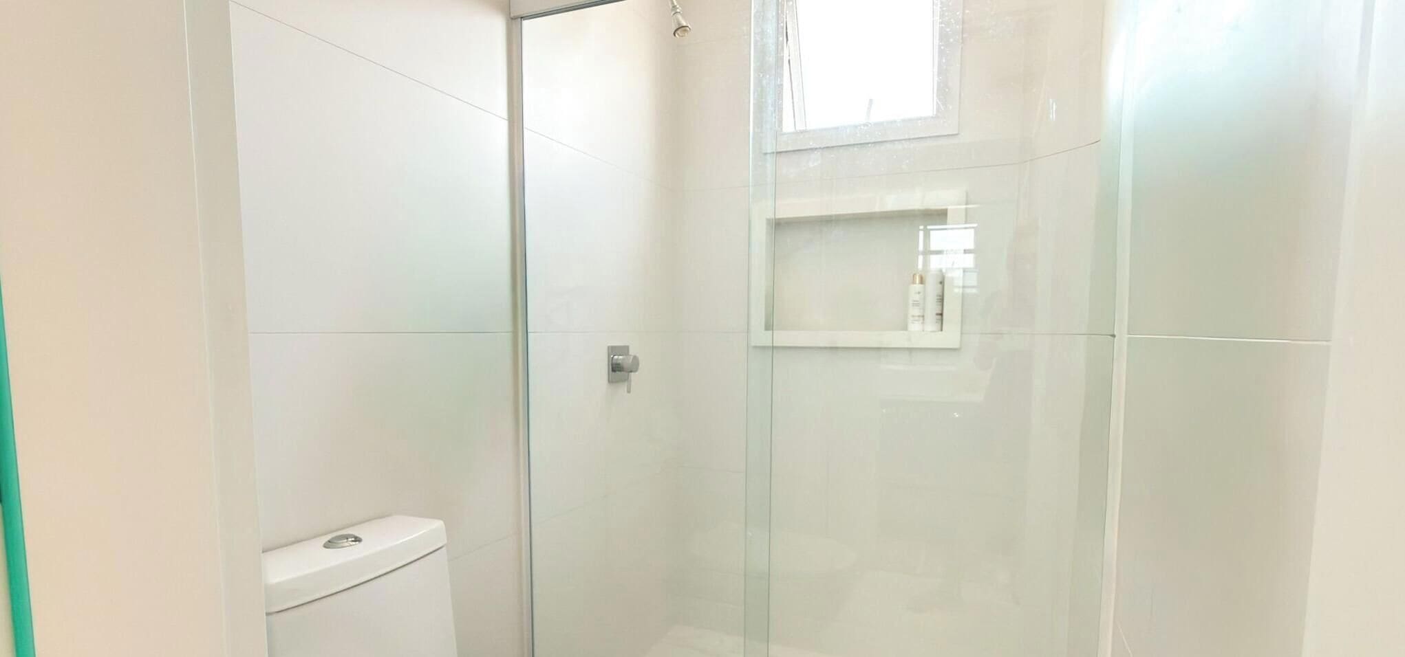 A bathroom with a glass shower enclosure, a toilet, and a small window.