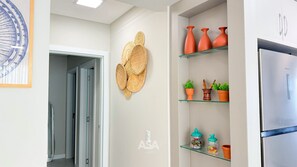 A kitchen with a refrigerator, shelves with potted plants, and a decorative wall piece. - ASA Vista Mar 3QT Alto Padrao Itapema (Itapema)