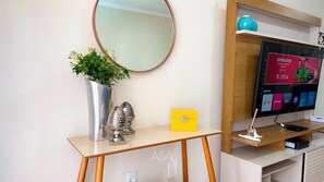 A reception desk with a mirror, a potted plant, decorative items, and a television displaying a sports channel. - ASA 3QT Leblon Ar Av. Brasil Centro BC (Balneário Camboriú)