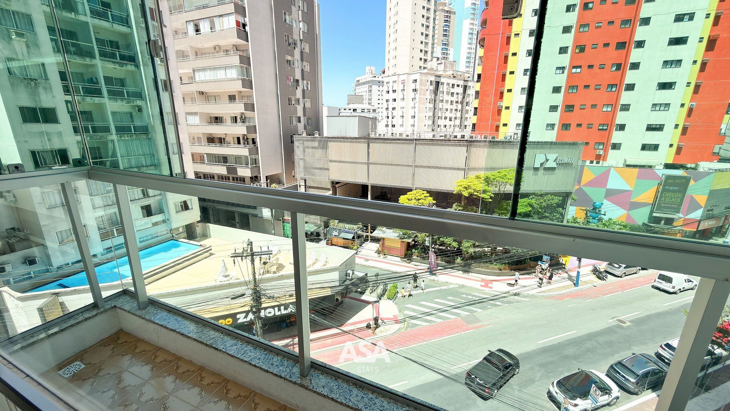A high-rise building with a glass balcony overlooking a street with cars and pedestrians.