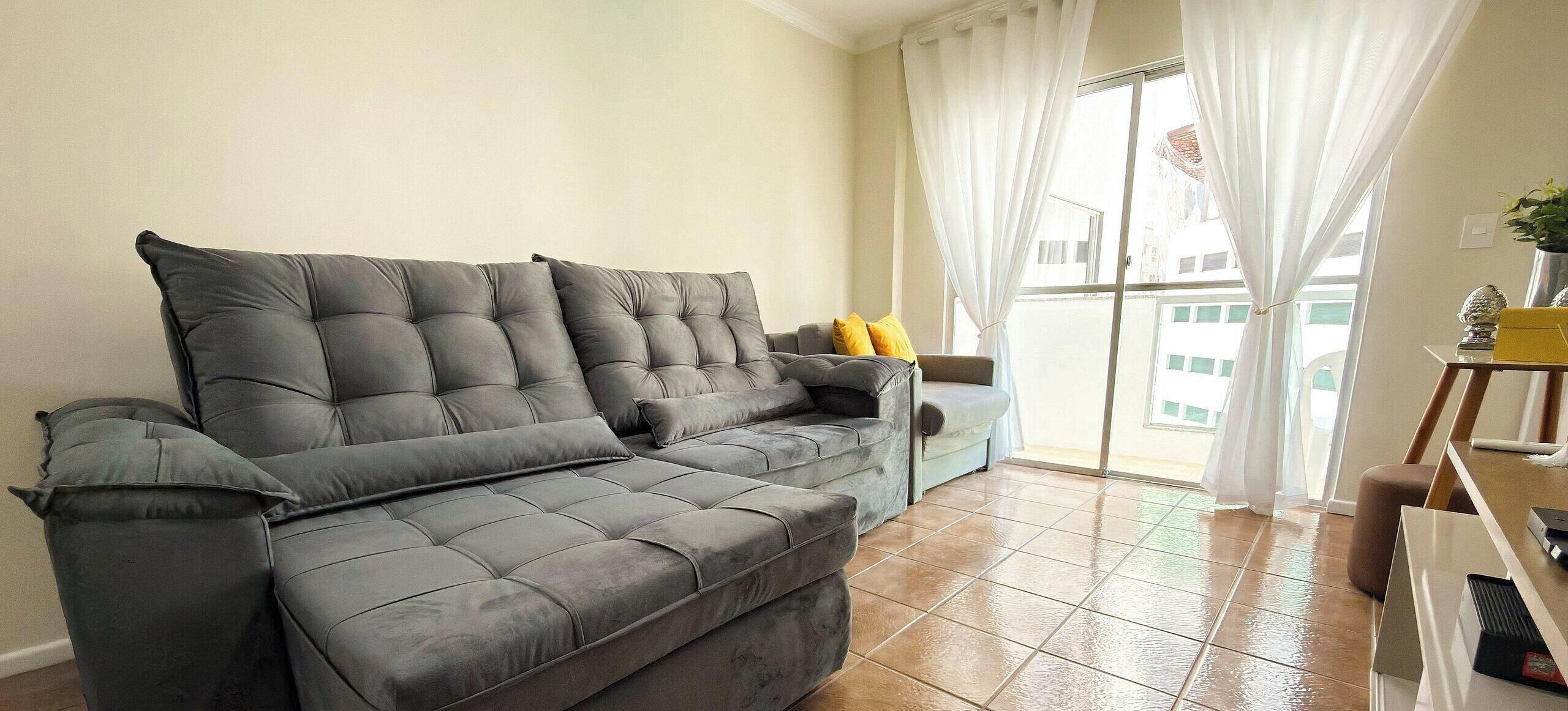 A grey sofa with multiple cushions, a small table with a plant, and a window with curtains.