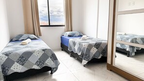 Quarto com três camas, cada uma com colcha e almofadas estampadas, um espelho grande e janela com vista para a cidade.