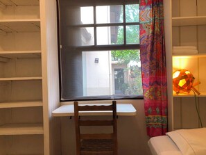 Una habitación con ventana, escritorio, silla, cama y lámpara.