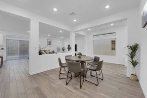 Een modern interieur met een ronde eettafel, grijze stoelen en een groot raam met zonwering.
