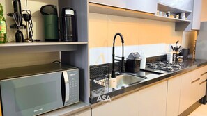 A modern kitchen with a built-in microwave, a sink with a faucet, and a stove. - ASA Valentina Apartment 2 Suites Itapema (Itapema)