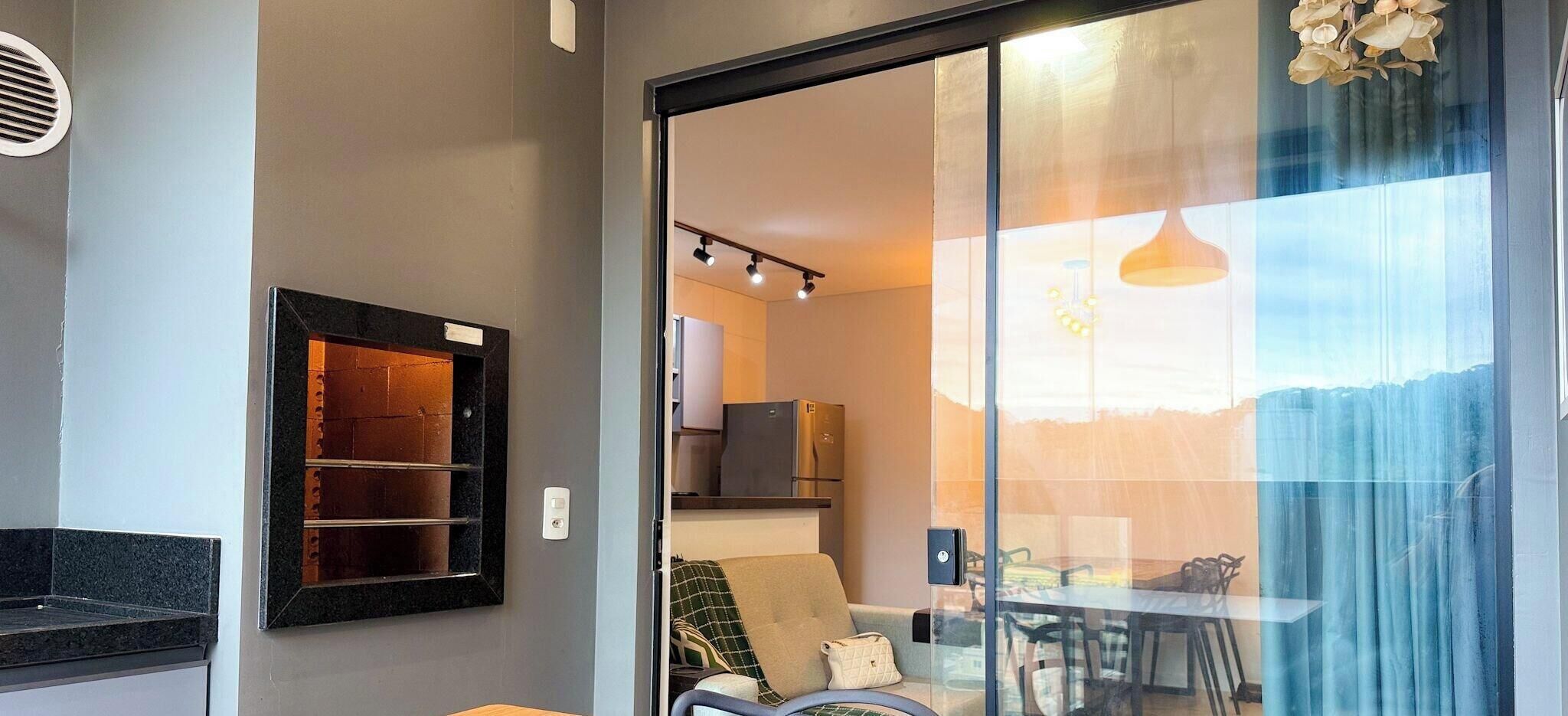 A modern interior with a sliding glass door leading to a dining area, a built-in shelf unit, and a visible kitchen area with appliances.