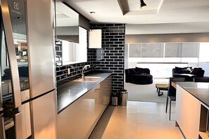 A modern kitchen with a black brick backsplash, stainless steel appliances, and a dining area with a black sofa and a small table. - ASA Apto de Alto Padrao Ed a Beira Mar Design (Balneário Camboriú)