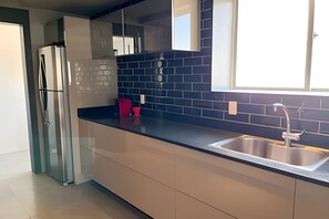 A modern kitchen with a stainless steel refrigerator, a black countertop, and a sink with a faucet. - ASA Apto de Alto Padrao Ed a Beira Mar Design (Balneário Camboriú)