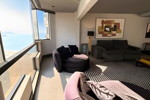 Ett modernt vardagsrum med ett stort fönster, en grå soffa, en svartvit mönstrad matta och ett minimalistiskt konstverk på väggen.