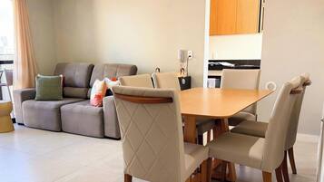 A modern living room with a sofa, a dining table with chairs, and a kitchen area in the background.