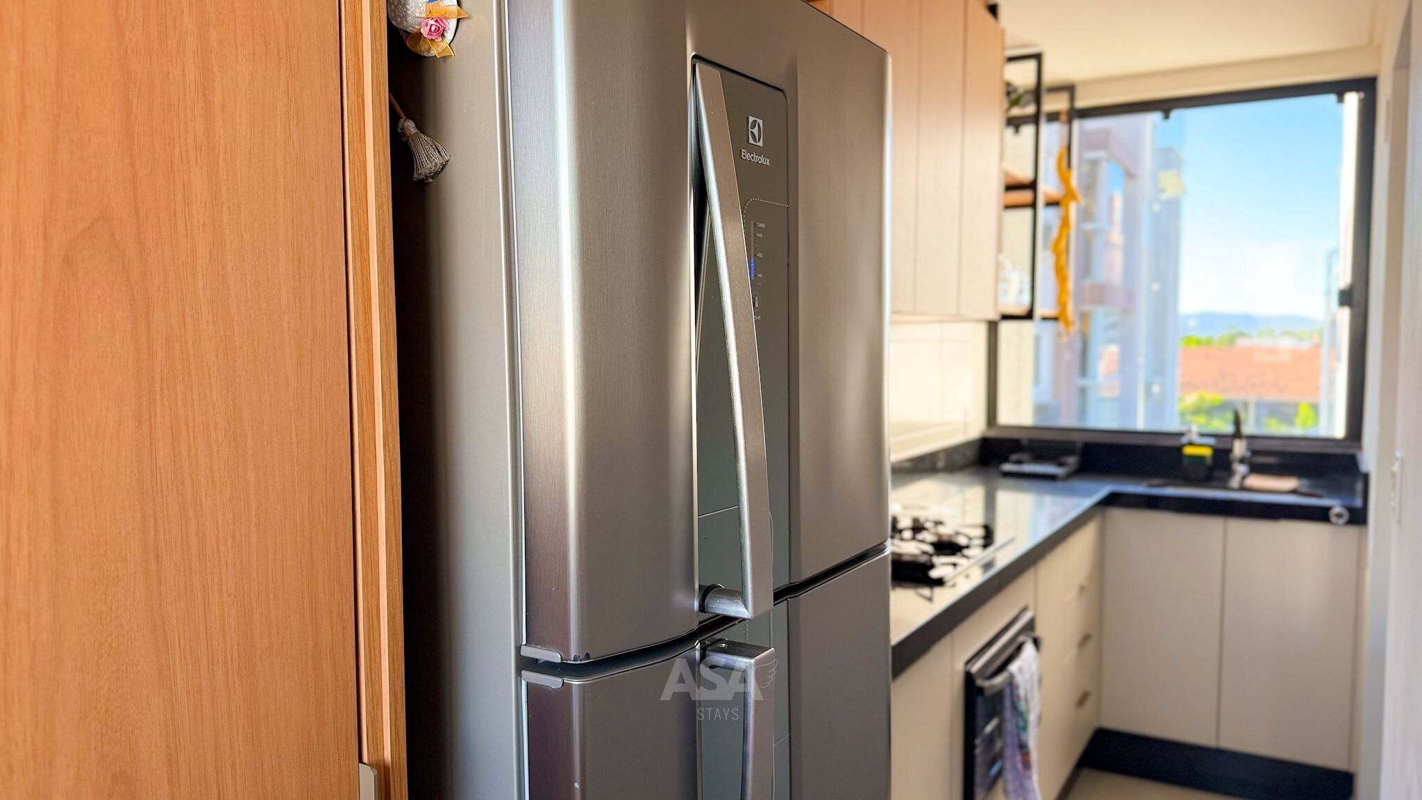 A stainless steel refrigerator in a kitchen with a window view.