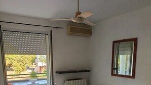 Un salon comprenant un canapé, une petite table, un ventilateur de plafond et une vue sur un espace extérieur aménagé avec des chaises et une table, accessible par une porte vitrée.