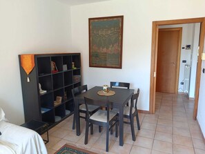 Een eethoek met een tafel, stoelen, een boekenkast en een schilderij aan de muur.