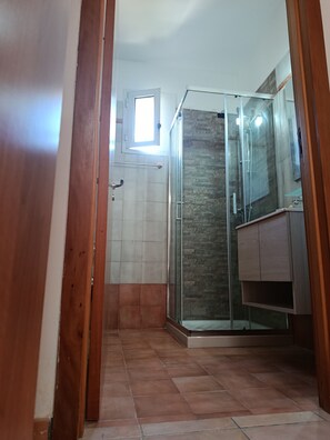 Een badkamer met een douchecabine van glas, een houten deur en een klein raam.
