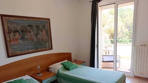 Une chambre avec deux lits, une table de chevet, une lampe, un tableau au mur et une porte-fenêtre coulissante donnant sur un espace extérieur.