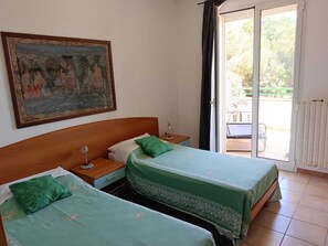 Een kamer met twee bedden, een nachtkastje, een lamp, een schilderij aan de muur en een schuifdeur naar een terras.