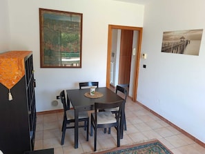 Ein Essbereich mit Tisch und Stühlen, einem Gemälde an der Wand und Blick durch eine geöffnete Tür.