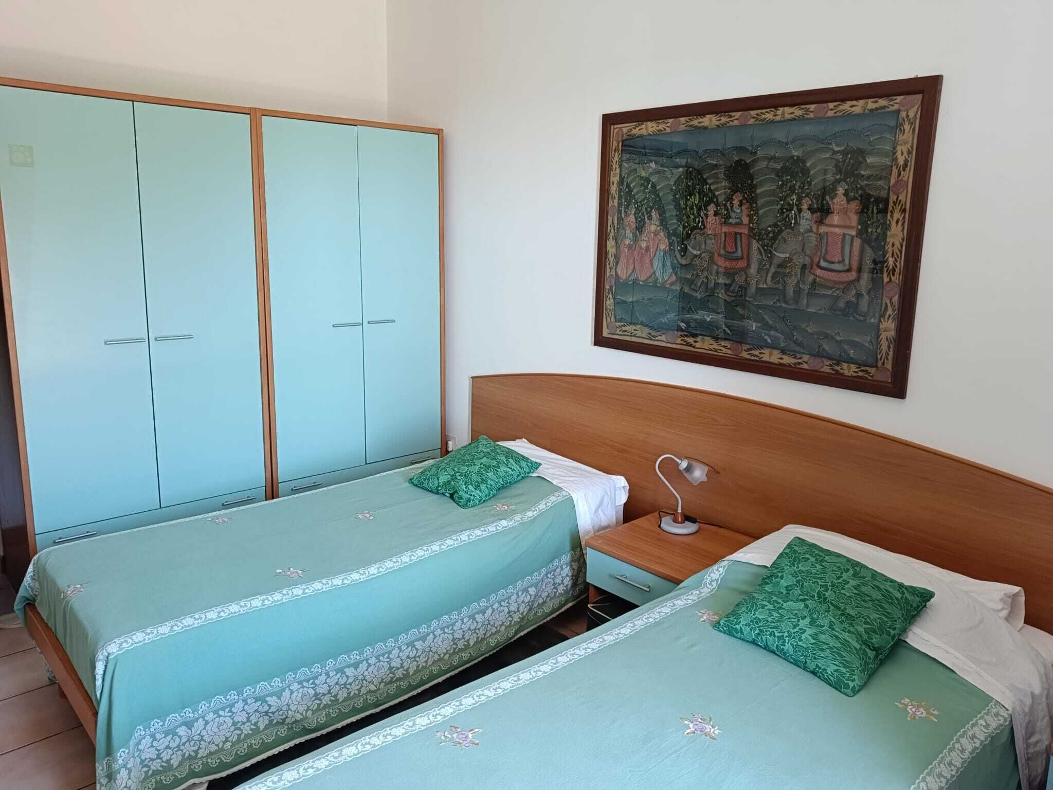 Una stanza con due letti singoli, un comodino con una lampada, un armadio e un quadro appeso al muro.
