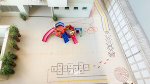Ein Kinderspielbereich mit Rutsche und Klettergerüsten, umgeben von Topfpflanzen.