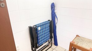 A room with a blue checkered item on a stand, a wooden chair, and a white tiled wall. - ASA Apto Central 2 QT Climatizado BC (Balneário Camboriú)