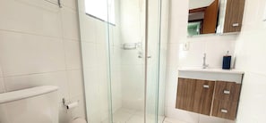 A modern bathroom with a glass shower enclosure, a toilet, and a vanity with a mirror and sink. - ASA Apto Confortavel Indaial 2 QT Garagem (Indaial)
