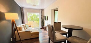 A living room with a sofa, chairs, a table, a lamp, and a TV. - ASA Apto Confortavel Indaial 2 QT Garagem (Indaial)