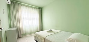 A room with a bed, a window with curtains, a radiator, and a wall-mounted air conditioner.