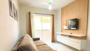 Una sala de estar con un sofá, un televisor montado en una pared de madera y un ventanal corredero que da a un área exterior.