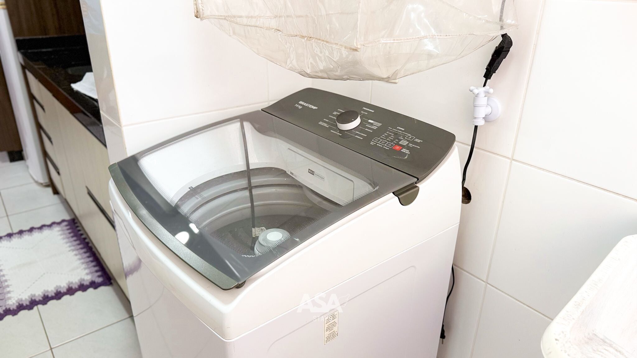 A front-loading washing machine with a control panel, a power cord, and a protective mesh cover.