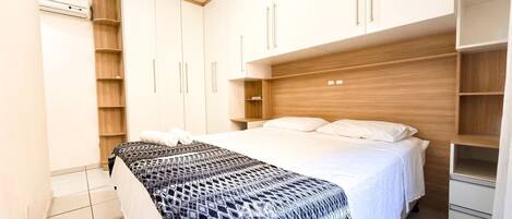 A bedroom with a bed, a bedside table, a wardrobe, and a built-in shelf.