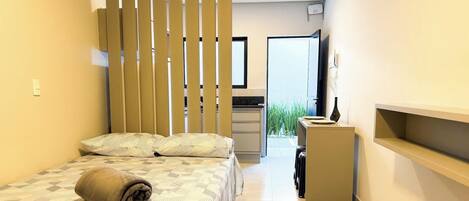 Une chambre d’hôtel de taille réduite, comprenant un lit, un bureau et une kitchenette.