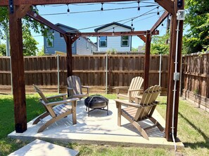 Una veranda riparata con poltrone Adirondack e un barbecue, circondata da un recinto in legno e case sullo sfondo.