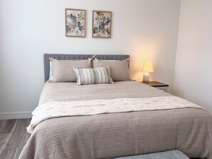 A neatly made bed with a grey headboard, a bedside lamp, and two framed artworks on the wall. - Modern 4BR Home • 5 Min Downtown & Fair Park (Dallas)