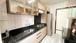 A kitchen with a black countertop, stainless steel sink, and a refrigerator. - ASA Apto Funcional Prox. Praia Centro BC (Balneário Camboriú)