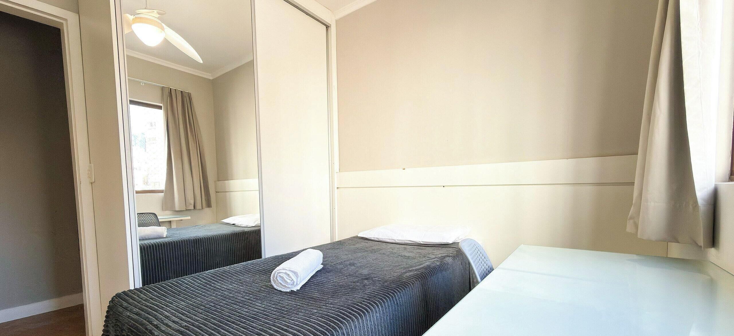 Une chambre d  ’hôtel avec deux lits, une fenêtre avec des rideaux, un ventilateur de plafond et un miroir.