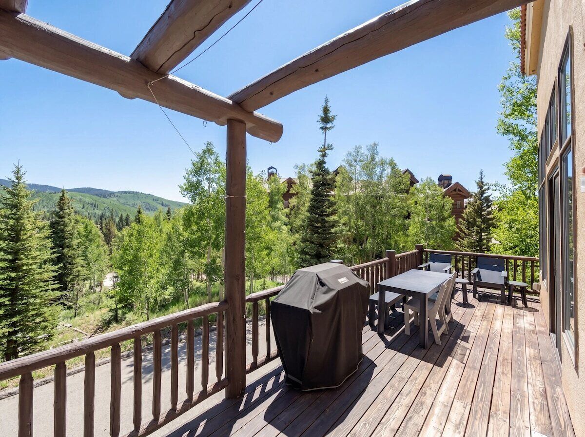 A wooden deck with outdoor furniture, a grill, and a view of a forested area.