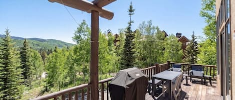 A wooden deck with outdoor furniture, a grill, and a view of a forested area.