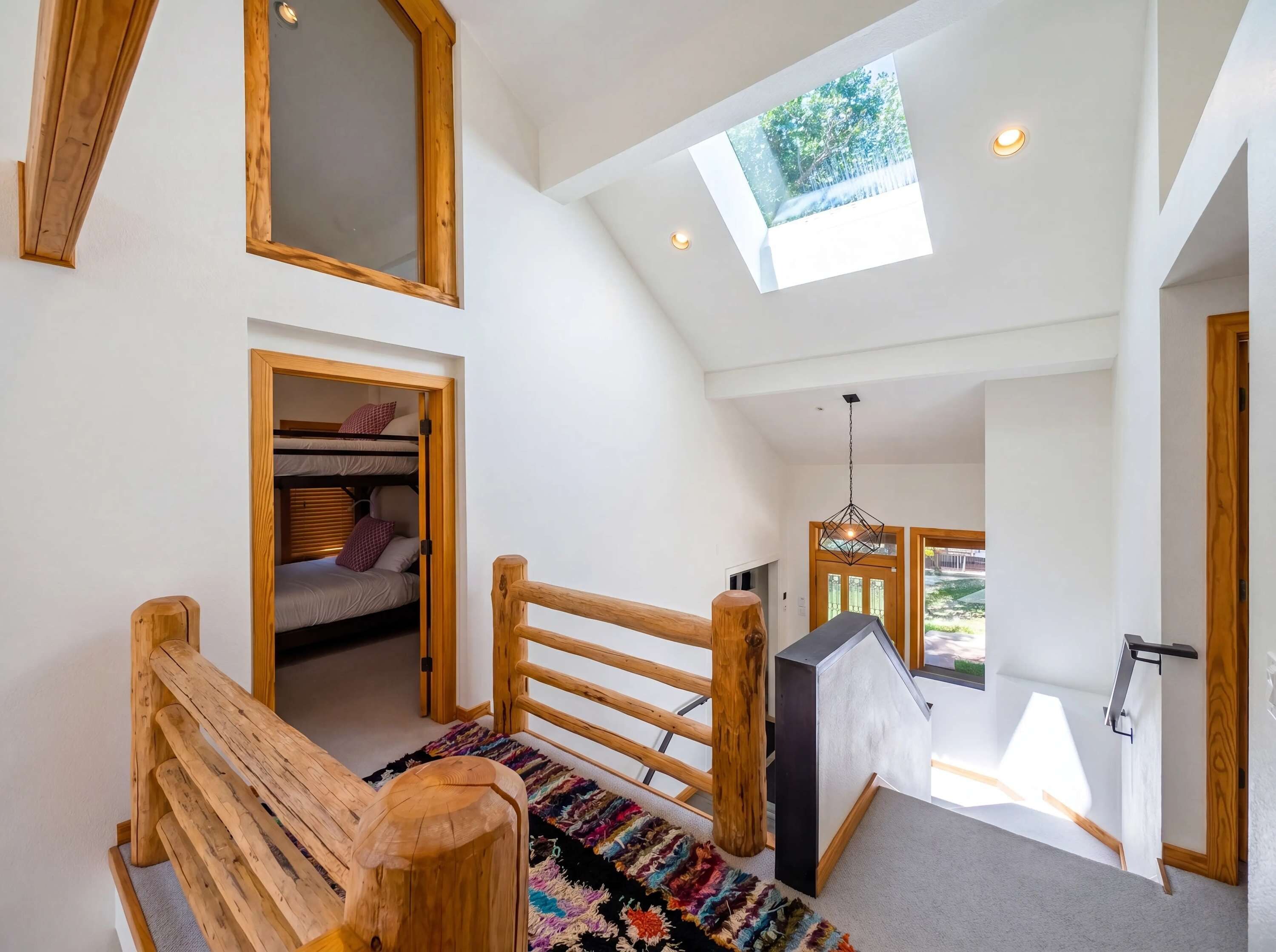 A loft bedroom with a skylight, bunk beds, a wooden bench, and a colorful rug.