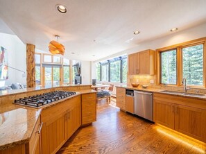 A modern kitchen with wooden cabinets, a central island, and a dishwasher. - Crystal Ridge | Stunning Views, Private Hot Tub, & Walk to Gondola/Village Core (Mountain Village)