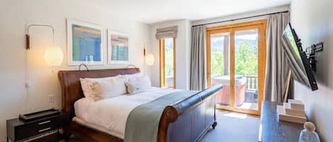 Un dormitorio con cama, mesitas de noche, escritorio y vistas al exterior.