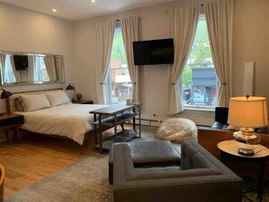 A hotel room with a bed, a sofa, a TV, a table, and a window with curtains. - Main Street Luxury in Heart of Telluride | Walk to Gondola and Explore Town (Telluride)